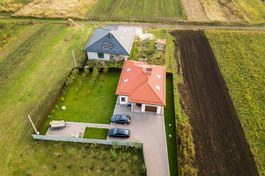 Çatı pencereleri ve yeşil çimenli asfalt avluda arabaları olan çatı kiremitli ev manzarası..
