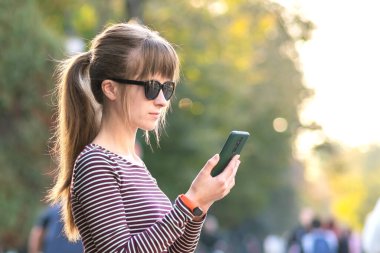 Genç ve güzel bir kadın sıcak yaz gününde cep telefonunu açık havada kullanıyor..