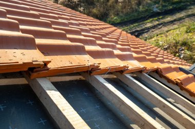 Üst üste binen sarı seramik çatı kiremitleri ahşap tahtalara monte edilmiş inşaat halindeki binanın çatısını kaplıyor..