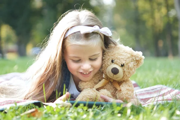 快乐的小女孩带着她最喜欢的玩具玩具玩具在夏天的公园里看手机 — 图库照片