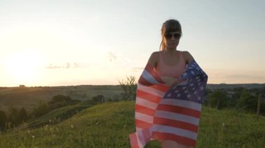 Gün batımında Amerikan bayrağıyla poz veren mutlu genç bir kadının arka görüntüsü. Amerika 'nın bağımsızlık gününü kutlayan pozitif kız. Uluslararası Demokrasi Günü.