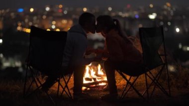 Genç bir çift, gece şenlik ateşinin yanında oturmuş sıcak romantik gecenin tadını çıkarıyor..