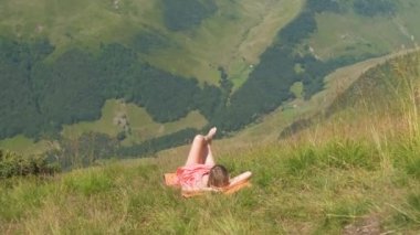 Kırmızı elbiseli genç bir kadın yeşil çimlere uzanıyor güneşli bir yaz gününde dinleniyor ve doğanın tadını çıkarıyor..