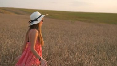 Kırmızı yaz elbisesi ve hasır şapkasıyla genç güzel bir kadın olgun altın buğdayla sarı tarlada yürüyor sıcak akşamın tadını çıkarıyor..