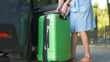 Genç kadın sürücü yeşil bavulu şehir caddesine koyuyor. Seyahat ve tatil kavramı.