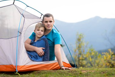 Oğlu ile birlikte yaz dağlarında kamp çadırında dinlenen genç bir baba. Aktif aile eğlencesi kavramı.