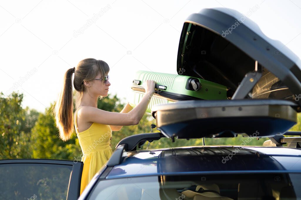Young woman taking green suitcase from car roof rack. Travel and vacations concept.