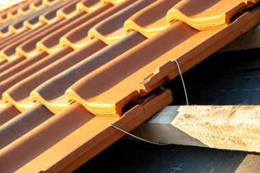 Ahşap tahtalara monte edilmiş sarı seramik çatı kiremitlerinin montajı için metal montaj çapasının kapatılması inşaat halindeki binanın çatısını kapsıyor..