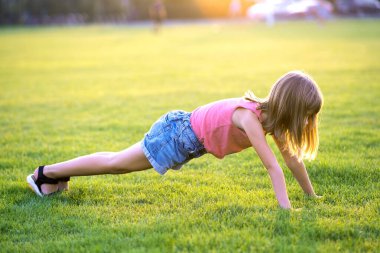 Genç ve güzel bir kız sıcak yaz akşamında yeşil çimlerde egzersiz yapıyor..