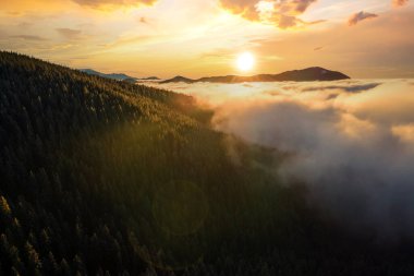 Sonbaharda yeşil ladin ormanlarıyla kaplı dağ tepelerinin üzerinde canlı gündoğumunun hava manzarası..