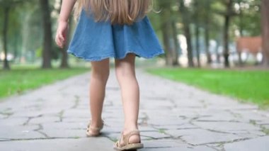 Yeşil parkta tek başına yürüyen yazlık elbiseli küçük bir kızın arka görüntüsü..