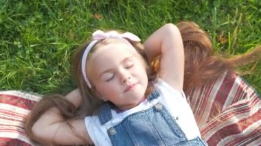 Güzel, küçük bir kız. Gözleri kapalı. Yazın yeşil çimlere uzanıp kestiriyor..