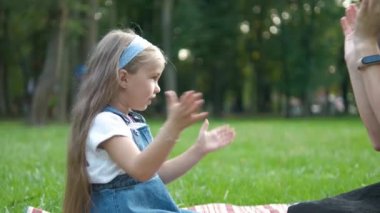 Güzel küçük kız annesiyle oyun oynuyor. Yeşil yaz parkında ellerini çırpıyor..