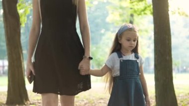 Anne ve uzun saçlı küçük kızı yaz parkında el ele yürüyorlar..