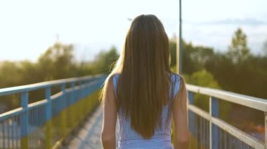 Gün batımında yaz parkında uzun saçlı genç bir kadının arka görüntüsü..