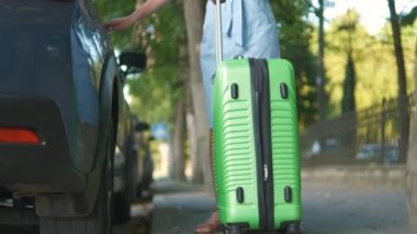 Genç kadın sürücü yeşil bavulu şehir caddesine koyuyor. Seyahat ve tatil kavramı.