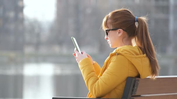 Jovem Mulher Bonita Sentada Banco Parque Navegando Seu Smartphone Livre — Vídeo de Stock