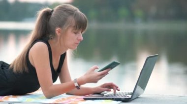 Kızgın kadın, dışarıda, yaz parkında dizüstü bilgisayarın arkasında çalışırken cep telefonuyla konuşuyor. Uzak çalışma konsepti.