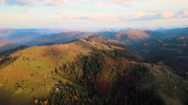 Günbatımında Ukrayna Karpatlar 'daki sonbahar ormanları arasında geniş çayırlardaki küçük çoban evlerinin havadan görünüşü.