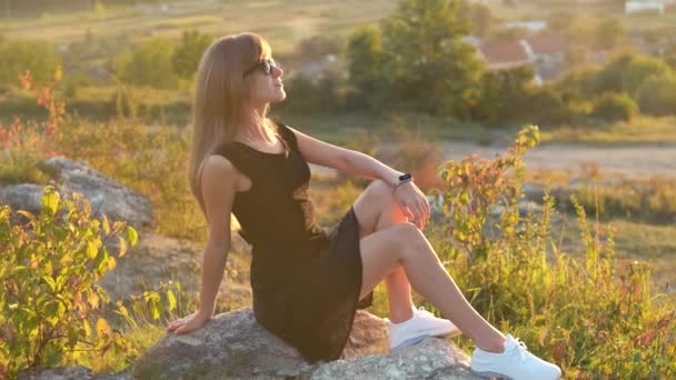 Молодая Элегантная Женщина Черном Коротком Платье Белых Кроссовках Сидит Скале — стоковое видео