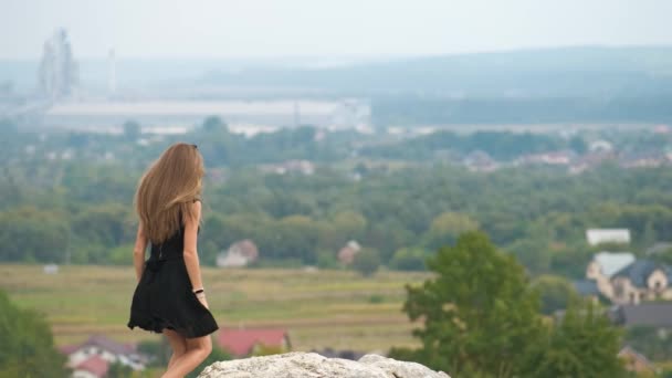 若いです幸せな女性で短い黒ドレス丘の上に立って暖かい夏の日を楽しむ — ストック動画