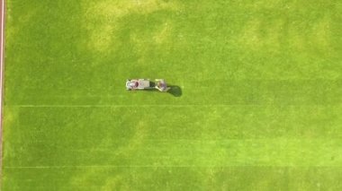 Küçük işçi figürünün havadan görünüşü yeşil çimenleri biçerek futbol stadyumu sahasında kırmızı koşu yolları ile mashine biçiyor..