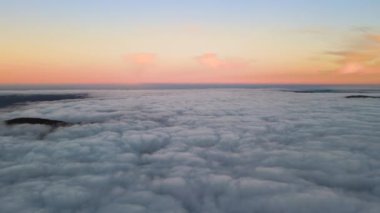 Ufuktaki uzak karanlık dağlarla beyaz yoğun bulutların üzerinde canlı gündoğumunun havadan görüntüsü..