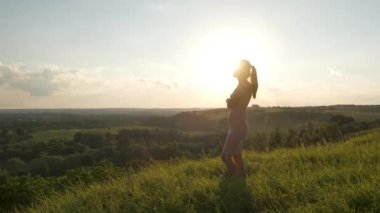 Yeşil tarlada duran genç bir kadın akşam doğasında günbatımının tadını çıkarıyor. Rahatlama ve meditasyon kavramı.