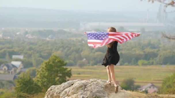 夏の暖かい日を楽しむ屋外でリラックス彼女の手の中に風のアメリカ国旗に手を振って長い髪を上げる若い幸せなアメリカ人女性 — ストック動画