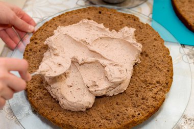 Evde kek pişirme süreci. Çikolatalı bisküvinin üzerine kadın el kreması dök. Mutfak ve lezzetli tatlı konsepti.