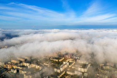 Modern şehrin üzerinde yüksek binaları olan kabarık beyaz bulutların üst hava manzarası.