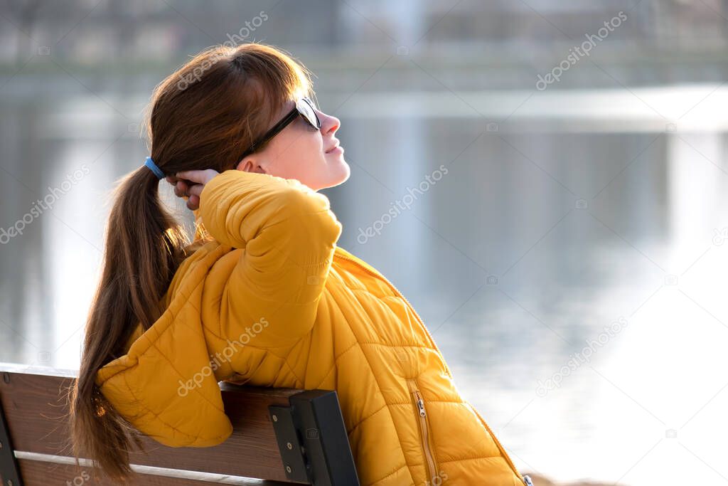 Young woman sitting alone on park bench relaxing on warm autumn day.