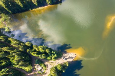 Yoğun yeşil ormanlarla kaplı yüksek dağ tepeleri arasında berrak mavi suyu olan büyük göl tepeden aşağıya doğru..