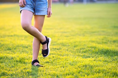 Sıcak yaz akşamında yeşil çimlerin üzerinde kot şortlu genç kız bacaklarının yakın çekimi..