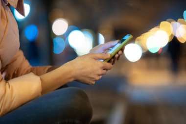Kadın ellerinin cep telefonu tutarak şehir caddesinde internet taraması yapması gece bulanık ışıklarla.