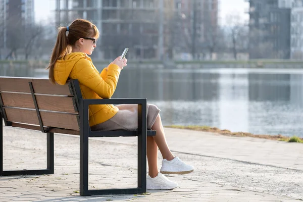 Молодая Красивая Женщина Сидит Скамейке Парке Просматривая Свой Смартфон Открытом — стоковое фото