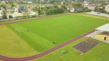 Küçük işçi figürünün havadan görünüşü yeşil çimenleri biçerek futbol stadyumu sahasında kırmızı koşu yolları ile mashine biçiyor..