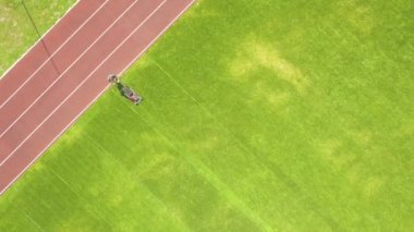 Küçük işçi figürünün havadan görünüşü yeşil çimenleri biçerek futbol stadyumu sahasında kırmızı koşu yolları ile mashine biçiyor..
