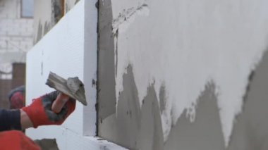 İnşaat işçisi ev duvarını yapışkan çimento yapıştırıcısıyla kaplıyor berore termal koruma için köpük yalıtım çarşafları yerleştiriyor..