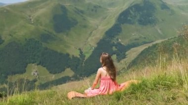 Kırmızı elbiseli genç bir kadın güneşli bir yaz gününde yeşil çimen tarlasında dinleniyor doğanın tadını çıkarıyor..
