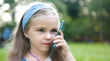 Mutlu küçük kız yaz parkında cep telefonuyla konuşuyor..