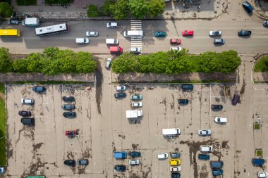Yoğun caddenin yukarıdan aşağı görüntüsü hareket halindeki arabaların trafiği ve park etmiş birçok aracın olduğu büyük otopark..