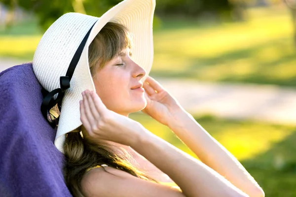 Young woman relaxing outdoors on sunny summer day. Happy lady lying down on comfortable beach chair daydreaming thinking. Calm beautiful smiling girl enjoying fresh air relaxing with closed eyes.