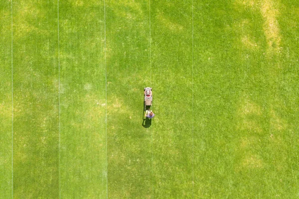 夏のサッカー競技場フィールド上の芝刈り機で緑の草をトリミング男労働者の小さな図の空中ビュー — ストック写真