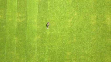 Yazın futbol sahasında çimenleri biçen ve çim biçen küçük işçi figürünün havadan görünüşü..