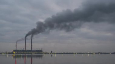 Kömür santrali yüksek borular siyah dumanlı geceleri hızlı hareket eden atmosferi gölün suyundaki yansımalarıyla kirletiyor. Günbegün zaman geçişi.
