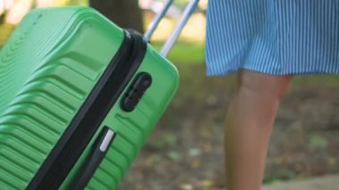 Genç bir kadının yaz günü yeşil bavuluyla kaldırımda yürümesi..