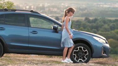 Kaputu açık, bozuk bir arabanın yanında duran genç bir kadın sürücü aracın motorunu kontrol ediyor ve yardım bekliyor..