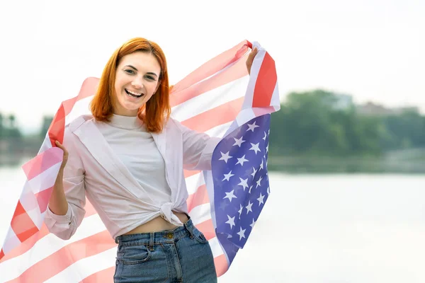 脸上挂着幸福笑容的红头发姑娘的画像 肩上挂着美国国旗 庆祝美国独立日的积极青年妇女 — 图库照片