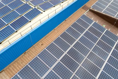 Sanayi binasının çatısına monte edilmiş mavi fotovoltaik panelleri olan güneş enerjisi santralinin hava görüntüsü.